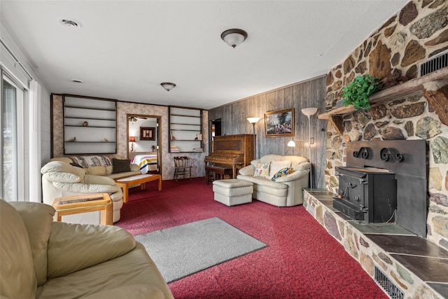 carpeted living room featuring a wood stove, wooden walls, and built in shelves