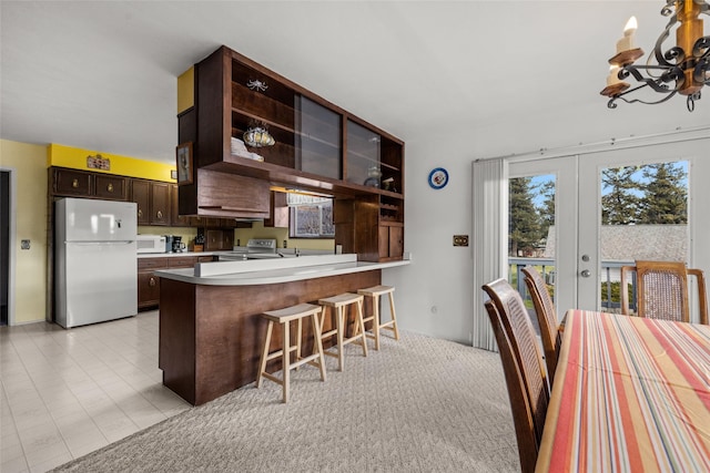 kitchen featuring kitchen peninsula, a breakfast bar, white appliances, dark brown cabinetry, and a notable chandelier