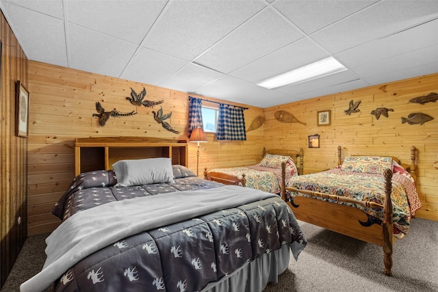 carpeted bedroom featuring a drop ceiling and wood walls