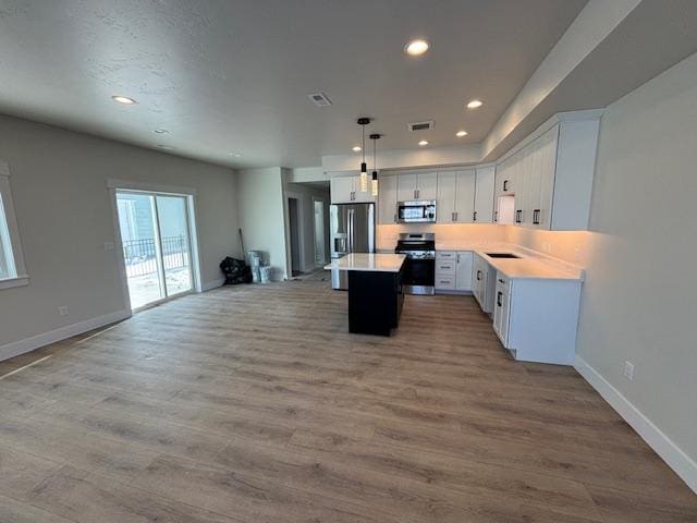 kitchen with a kitchen island, appliances with stainless steel finishes, decorative light fixtures, white cabinetry, and light hardwood / wood-style flooring