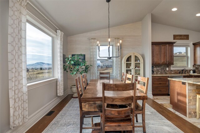 dining room with a mountain view, a healthy amount of sunlight, light wood-type flooring, and lofted ceiling