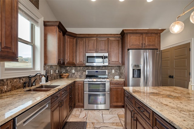 kitchen featuring stainless steel appliances, light stone counters, hanging light fixtures, and sink