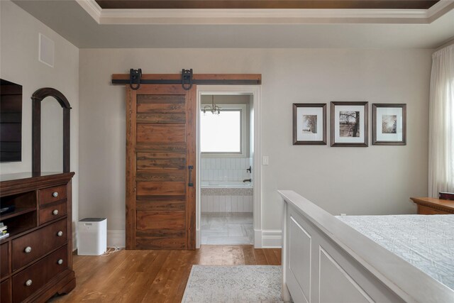 bedroom with a raised ceiling, a barn door, crown molding, ensuite bathroom, and light hardwood / wood-style floors