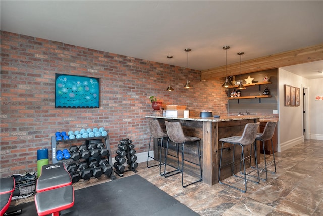 bar with light stone countertops, hanging light fixtures, and brick wall