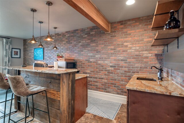 bar featuring sink, hanging light fixtures, light stone countertops, beam ceiling, and brick wall