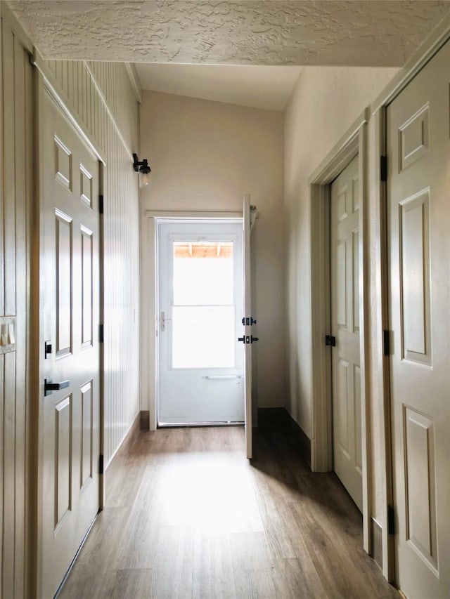 doorway to outside with a textured ceiling, light hardwood / wood-style flooring, and lofted ceiling