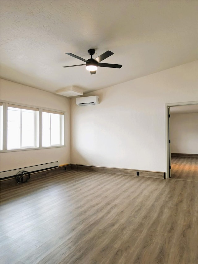 spare room with hardwood / wood-style flooring, ceiling fan, an AC wall unit, and a baseboard heating unit