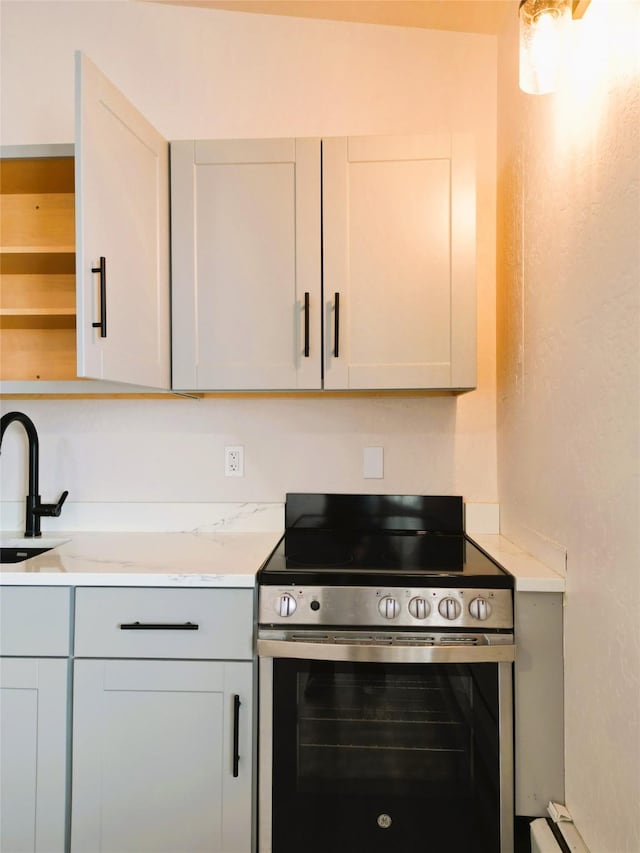 kitchen featuring electric range, light stone counters, white cabinets, and sink