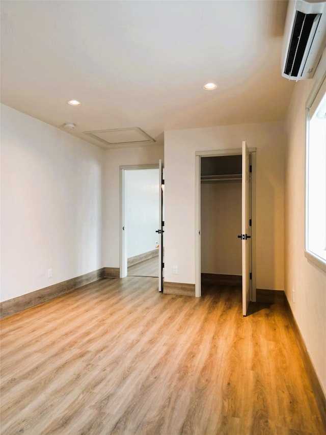 unfurnished bedroom featuring multiple windows, a wall mounted air conditioner, and light wood-type flooring