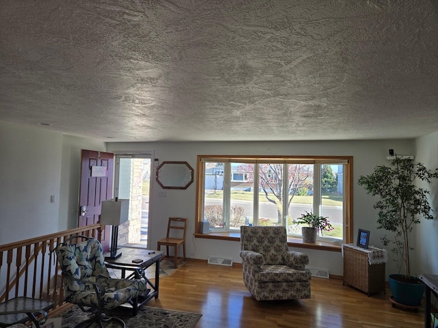 sitting room with visible vents, a textured ceiling, an upstairs landing, and wood finished floors