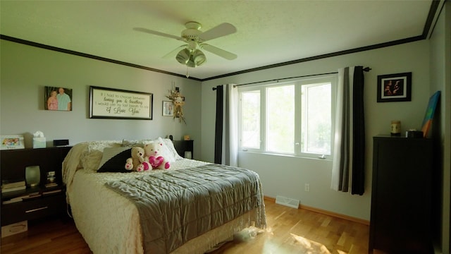 bedroom featuring visible vents, ornamental molding, a ceiling fan, wood finished floors, and baseboards