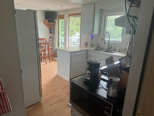 kitchen featuring light countertops, light wood-style floors, freestanding refrigerator, white dishwasher, and a peninsula