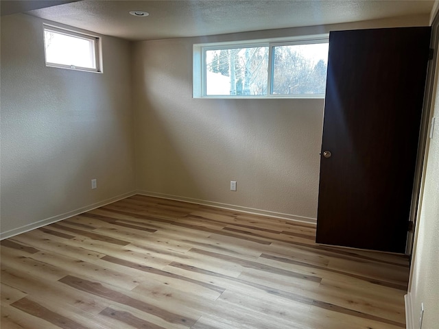 interior space featuring baseboards, a textured wall, a textured ceiling, and light wood finished floors