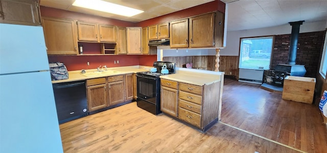 kitchen with sink, light hardwood / wood-style floors, a wood stove, and black appliances