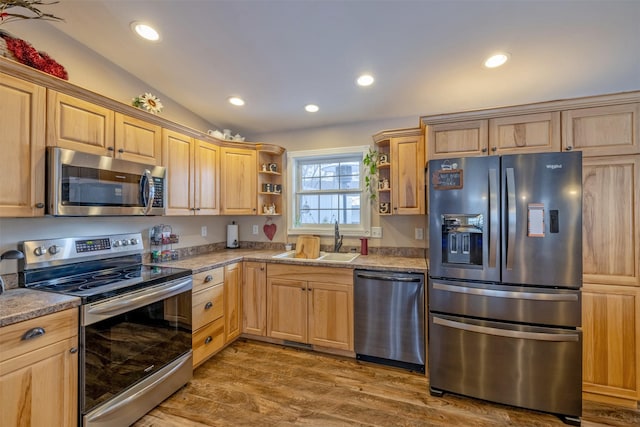 kitchen with light stone countertops, sink, vaulted ceiling, appliances with stainless steel finishes, and hardwood / wood-style flooring