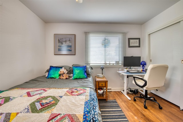 bedroom with a closet, hardwood / wood-style floors, and a baseboard heating unit