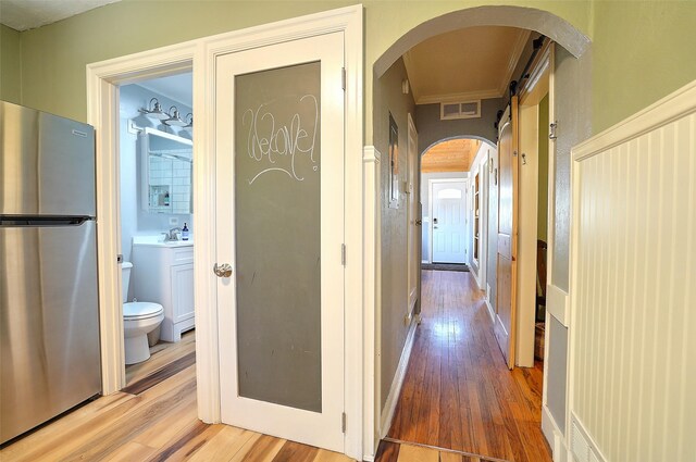 hallway with a barn door, sink, ornamental molding, and hardwood / wood-style flooring