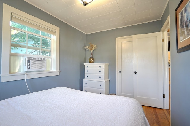 bedroom with hardwood / wood-style floors, cooling unit, crown molding, and a closet