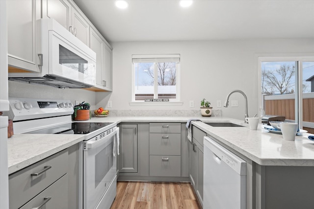 kitchen with light stone countertops, sink, light hardwood / wood-style flooring, kitchen peninsula, and white appliances