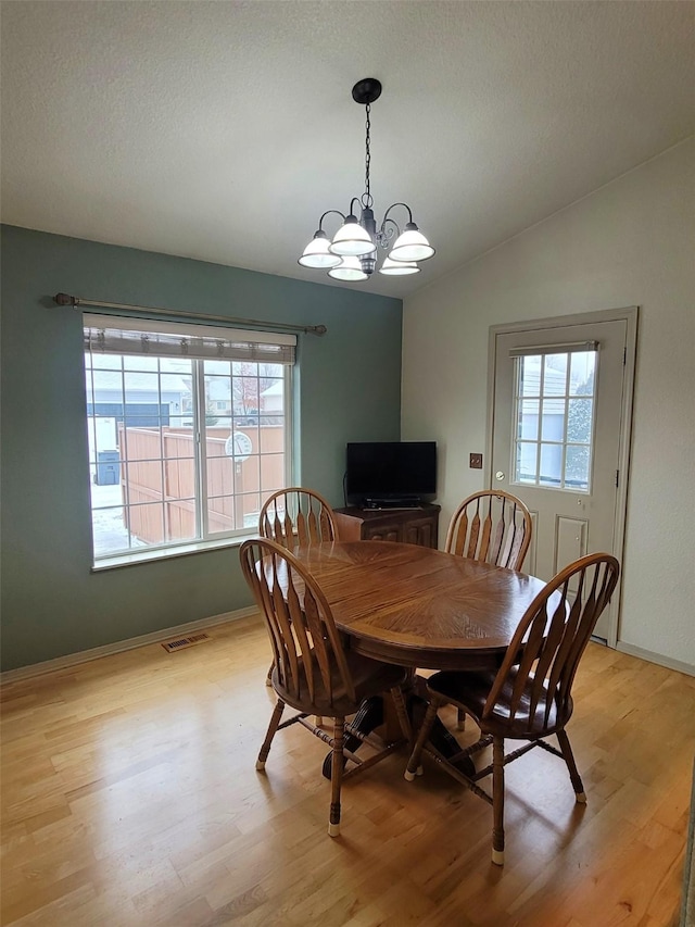 dining area featuring an inviting chandelier, lofted ceiling, a textured ceiling, and light hardwood / wood-style flooring