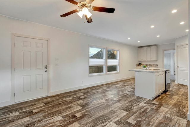 kitchen with light stone countertops, ceiling fan, dark wood-type flooring, sink, and a center island with sink