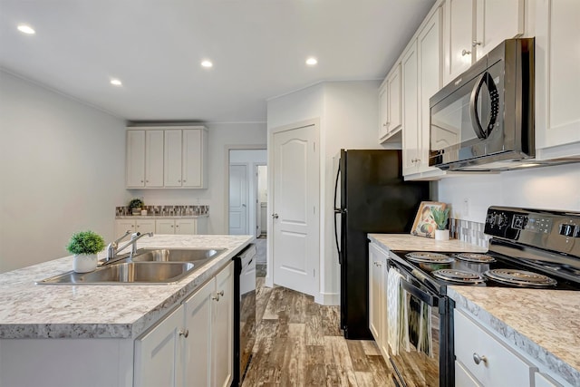 kitchen with a kitchen island with sink, sink, black appliances, light hardwood / wood-style flooring, and white cabinetry