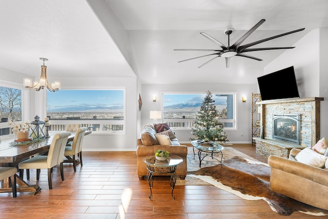 living room featuring ceiling fan with notable chandelier, hardwood / wood-style flooring, a stone fireplace, and lofted ceiling