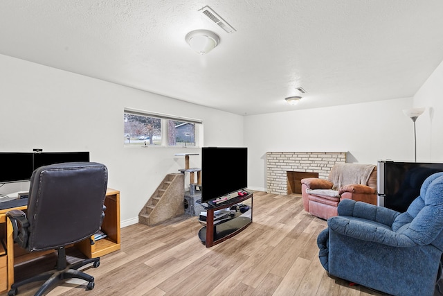 office space featuring light hardwood / wood-style floors, a textured ceiling, and a brick fireplace