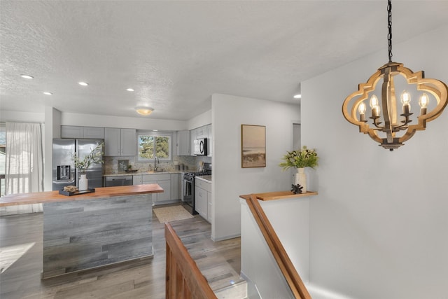 kitchen with hanging light fixtures, stainless steel appliances, light hardwood / wood-style floors, a textured ceiling, and gray cabinets