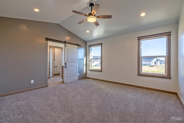 unfurnished bedroom with a barn door, ceiling fan, light carpet, and vaulted ceiling