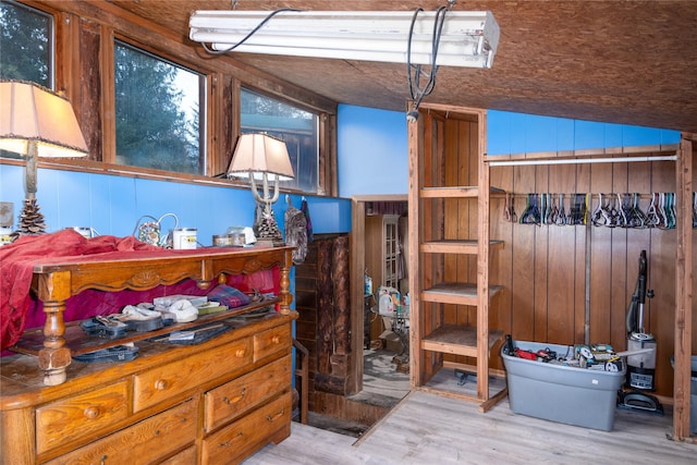 bedroom featuring wooden walls, light hardwood / wood-style floors, and vaulted ceiling