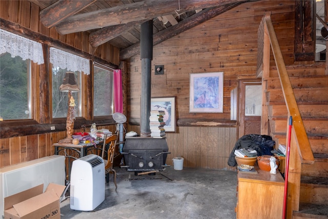 interior space with a wood stove, wooden ceiling, vaulted ceiling with beams, wood walls, and concrete floors