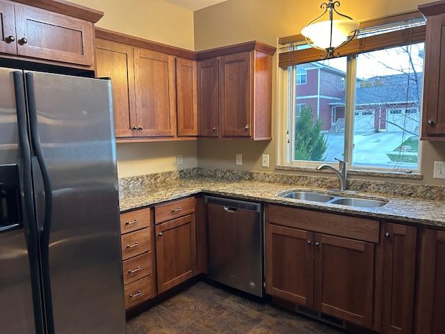 kitchen featuring light stone countertops, appliances with stainless steel finishes, decorative light fixtures, and sink