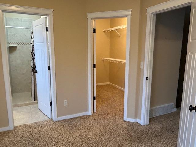 unfurnished bedroom featuring connected bathroom, a spacious closet, a closet, and light colored carpet