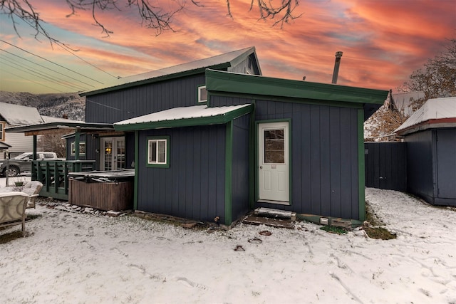 snow covered back of property with a hot tub