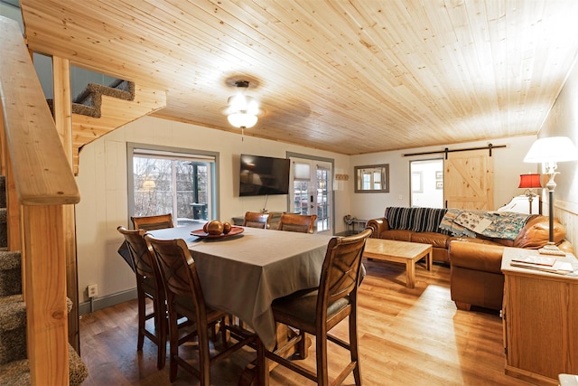 dining area featuring a barn door, light wood-type flooring, and wooden ceiling