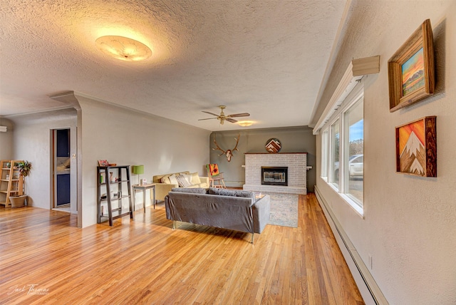 living area with a fireplace, a baseboard radiator, light wood-style flooring, ceiling fan, and a textured ceiling