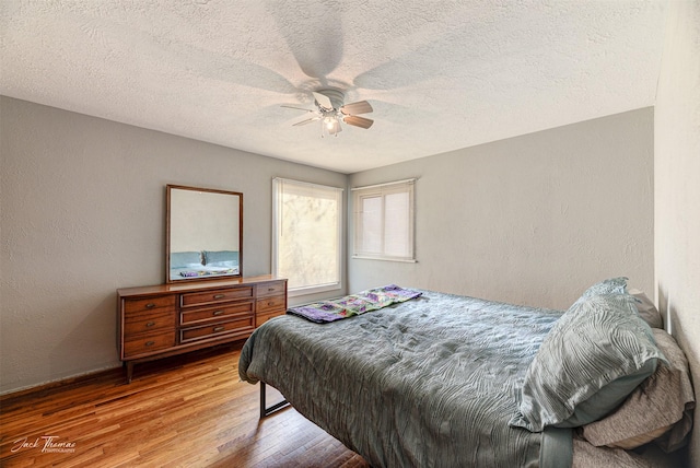 bedroom featuring a textured ceiling, a textured wall, wood finished floors, and a ceiling fan