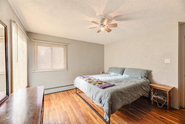 bedroom with ceiling fan, a textured ceiling, baseboard heating, and wood finished floors