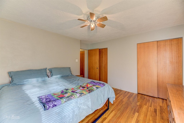 bedroom featuring a ceiling fan, a textured ceiling, light wood finished floors, and two closets