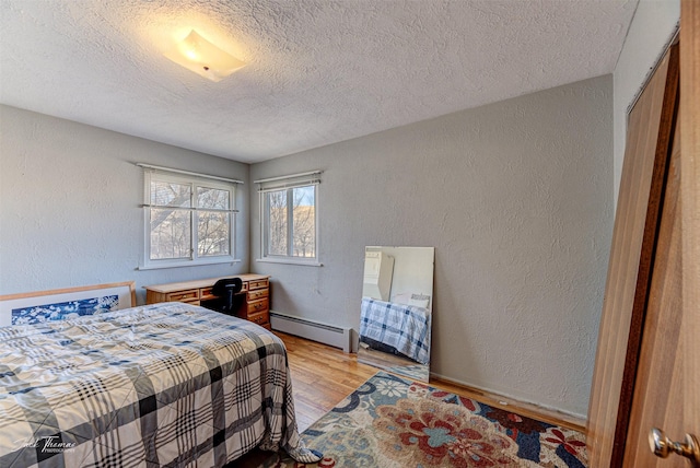 bedroom with light wood-style floors, a baseboard radiator, a textured wall, and a textured ceiling