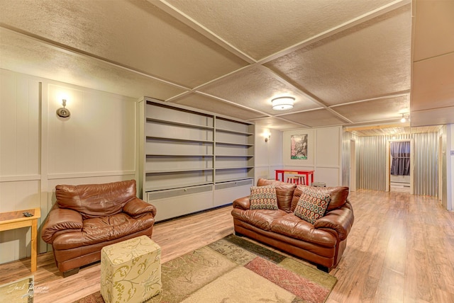 living area with built in shelves, a decorative wall, a textured ceiling, and wood finished floors