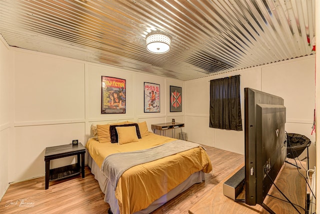 bedroom with light wood-style floors, wooden ceiling, and a decorative wall