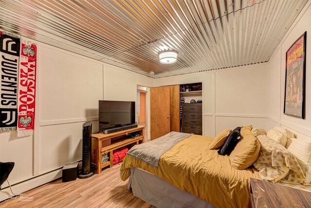 bedroom featuring a closet, light wood-type flooring, wood ceiling, and a baseboard radiator