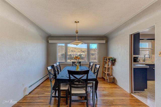 dining room with a baseboard heating unit, a textured wall, ornamental molding, and wood finished floors