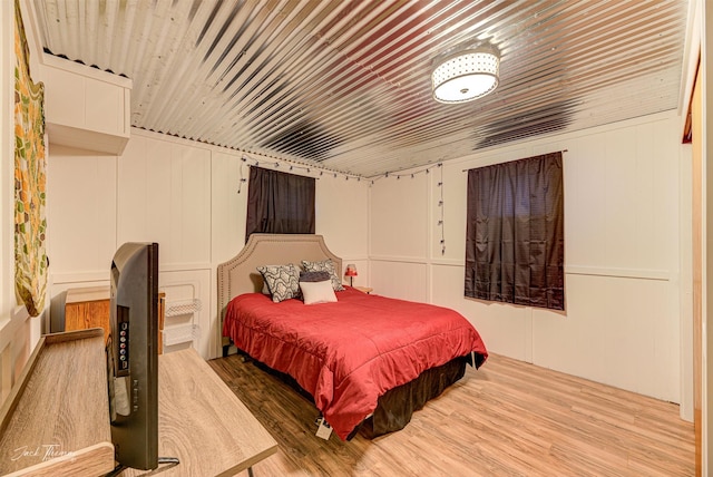 bedroom featuring wooden ceiling, wood finished floors, and a decorative wall