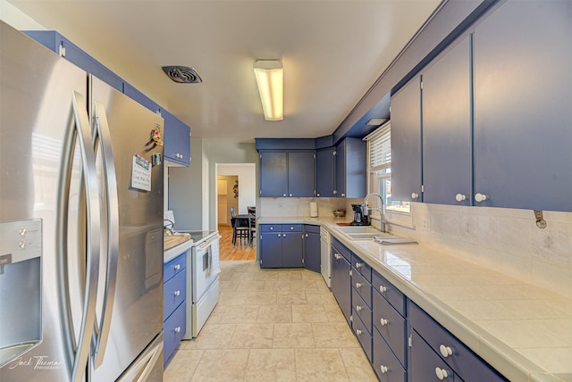 kitchen featuring blue cabinetry, tile counters, tasteful backsplash, a sink, and white appliances