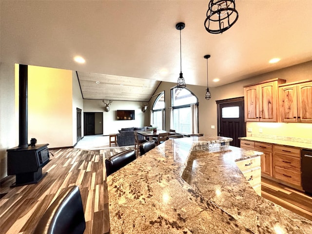 kitchen featuring lofted ceiling, hardwood / wood-style floors, hanging light fixtures, a wood stove, and light stone counters