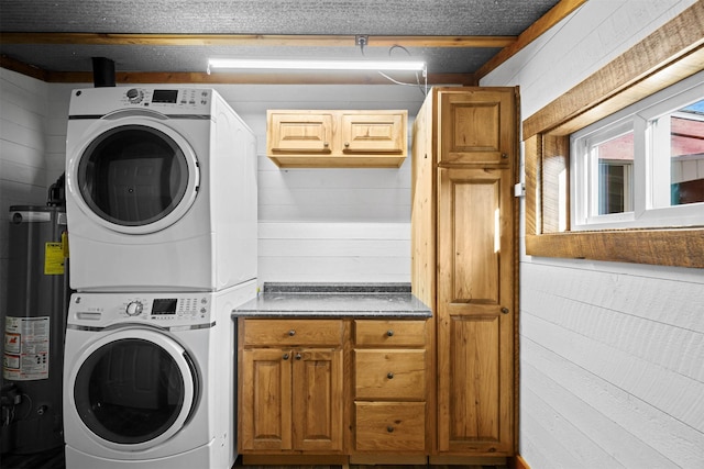 laundry room featuring cabinets, gas water heater, stacked washer and clothes dryer, and wood walls