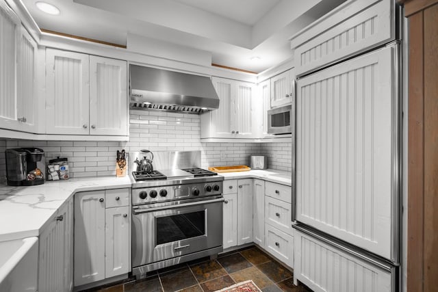2120 Iron Horse Dr Unit 11, Whitefish, MT 59937 - kitchen with premium appliances, wall chimney range hood, stone tile flooring, decorative backsplash, and light stone counters